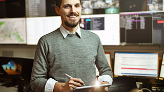 Ein Mann schreibt auf einem Tablet, im Hintergrund sind Computerarbeitspltze zu sehen