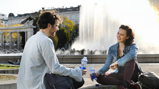 Frau und Mann sitzen mit Trinkwasserflaschen vor einem Brunnen