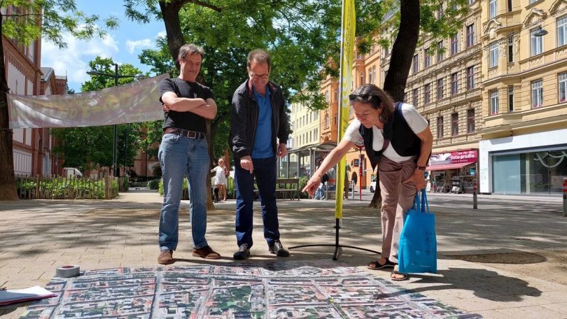 2 Männer und 1 Frau schauen auf einen überdimensionalen Stadtplan am Boden