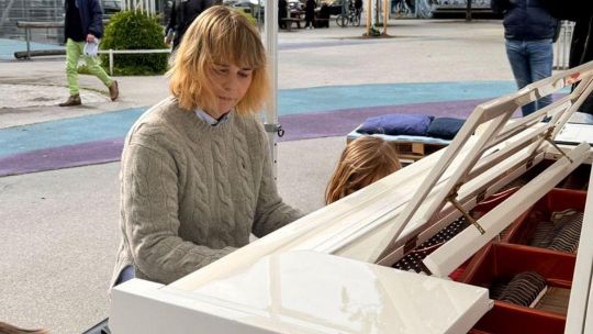 Frau spielt auf weißem Klavier im öffentlichen Raum