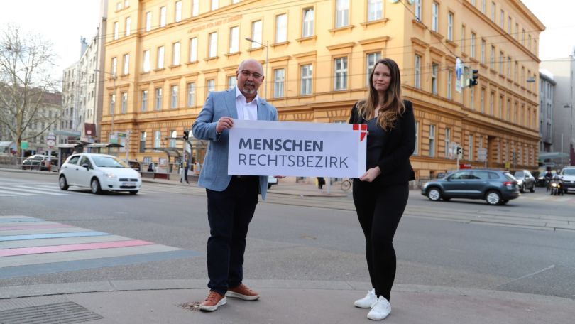 copyright: BV 21 2 Personen halten ein Schild mit "Menschenrechtsbezirk" an einer Kreuzung vor einem historischen Gebäude