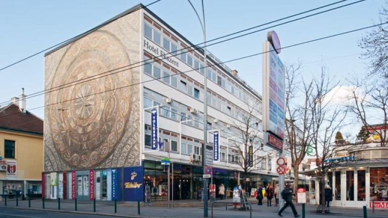 copyright: ©Pez Hejduk Schrägansicht eines länglichen 5-geschoßigen Baukörpers, auf der Schmalseite ein vollflächiges kreisförmiges Mosaik