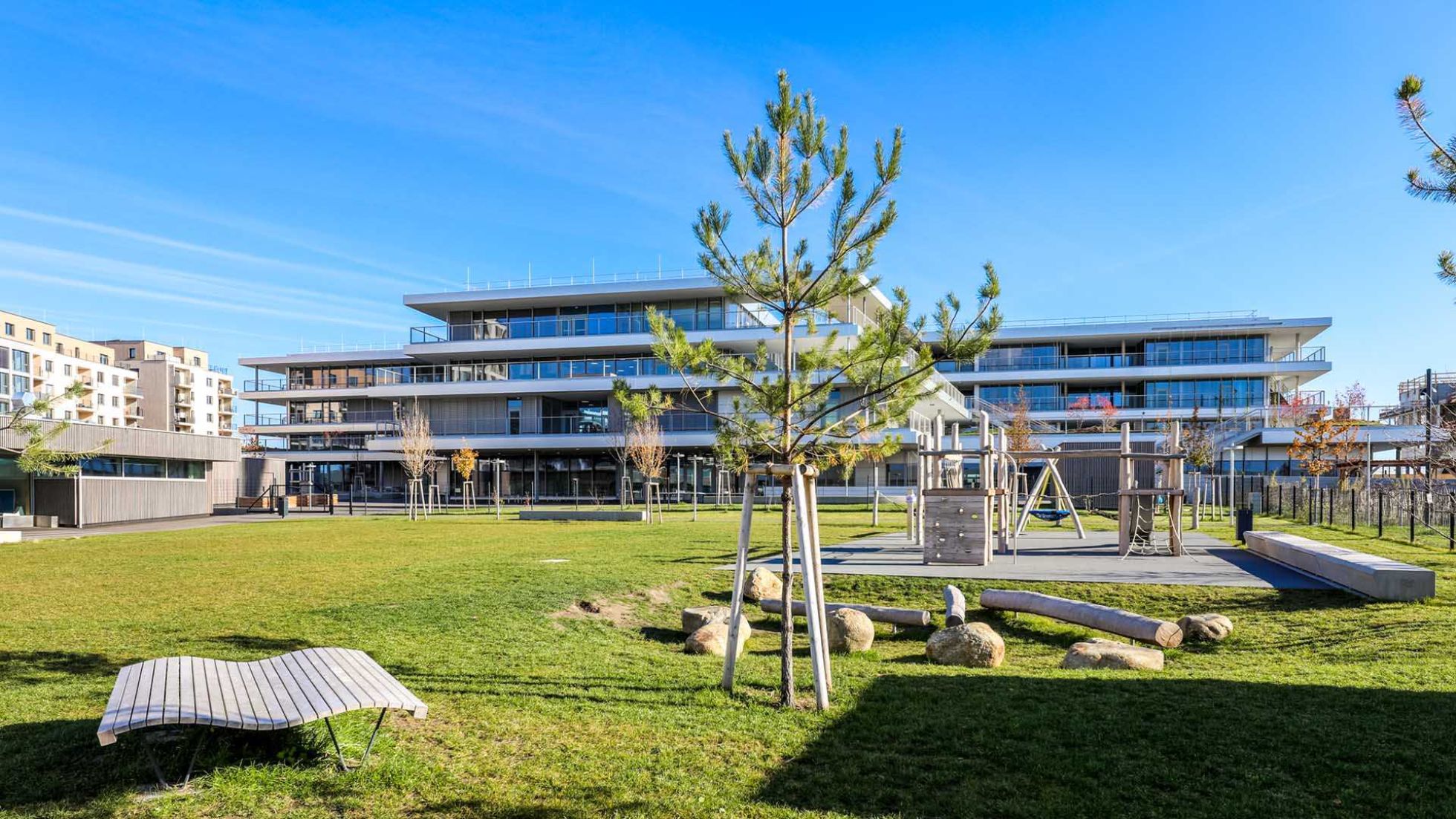 copyright: MA19/Christian Fürthner Rasen mit Liegefläche, Baum und großen Steinen als Sitzgelegenheit hinter Schulgebäude