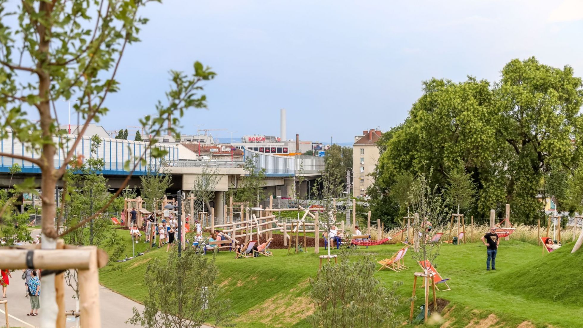 Grünraum mit Wiese, Bäumen, Sitzgelegenheiten und Spielplatz