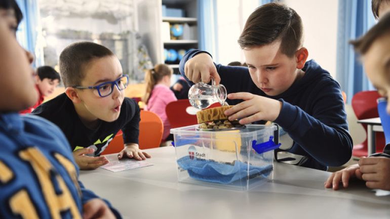 copyright: MA31 / Johannes Zinner Ein Junge leert Wasser auf einen Schwamm, 3 andere Jungen sehen dabei zu