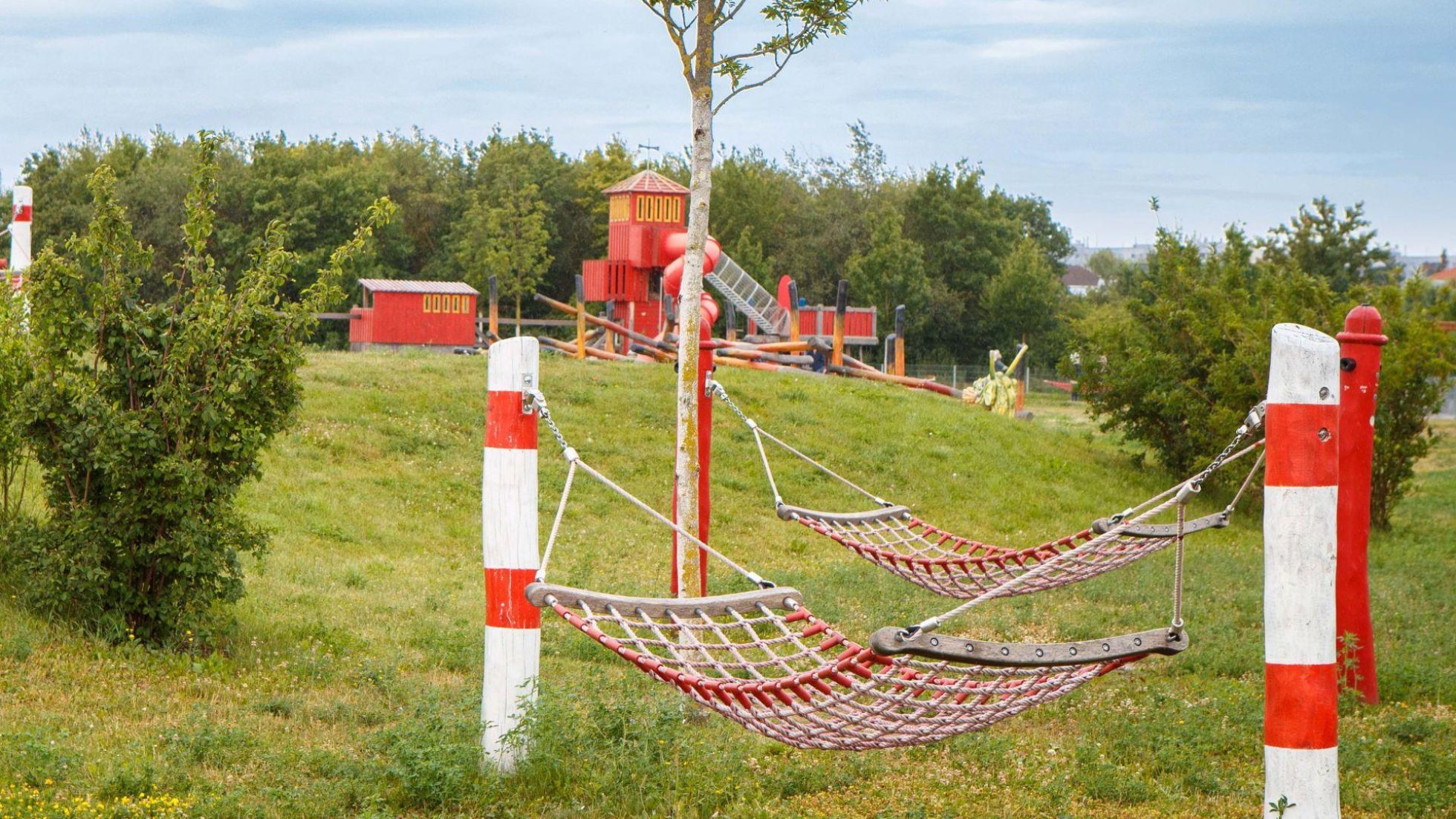 copyright: Stadt Wien/Houdek 2 Hängematten auf einer Wiese, im Hintergrund Feuerwehrspielgeräte auf einem Spielplatz.