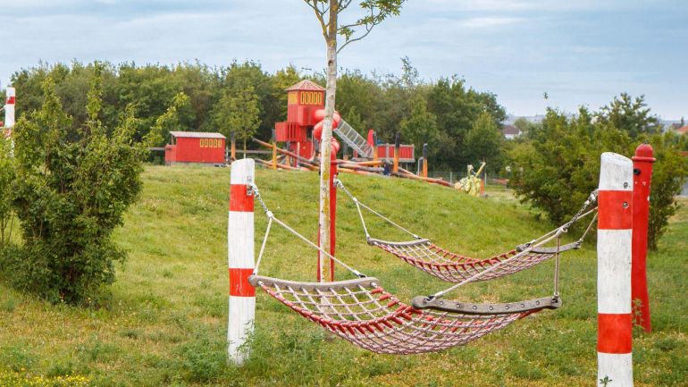 copyright: Stadt Wien/Houdek 2 Hängematten auf einer Wiese, im Hintergrund Feuerwehrspielgeräte auf einem Spielplatz.