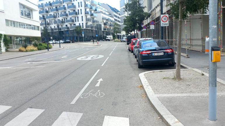 copyright: MA 46 Auf einer Straße mit Tempo 30 ist ein Mehrzweckstreifen auf der Fahrbahn eingezeichnet. Auf der rechten Straßenseite parken Autos.