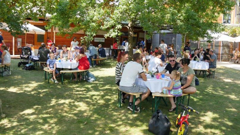 Familien sitzen an Tischen im Grümen