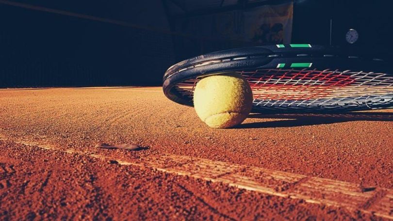 copyright: Pexels.com - Tookapic Tennisball und Tennisschläger auf rotem Sandboden