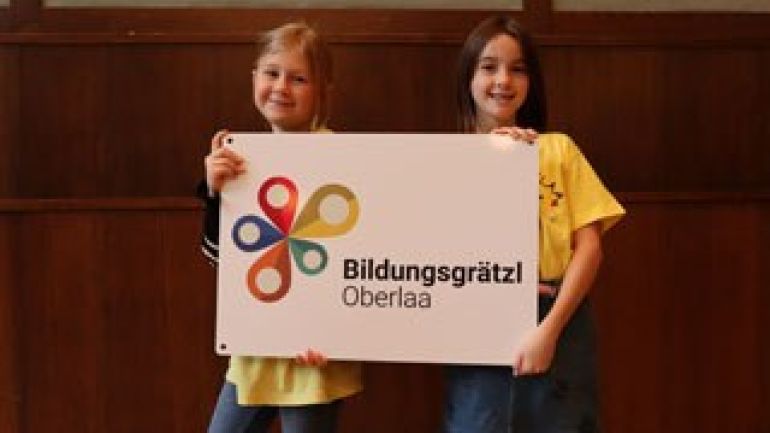 copyright: Stadt Wien/Markus Wache 4 Schüler*innen halten ein Schild mit Schriftzug "Bildungsgrätzl VerteilerKREIS"