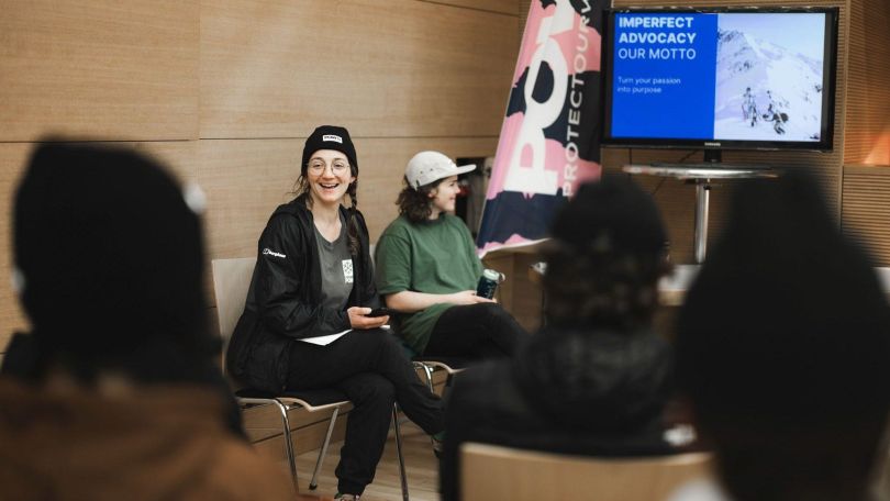 copyright: Miriam Knoll Zwei junge Frauen sitzen in lässiger Kleidung vor einer Gruppe von Menschen und halten einen Vortrag
