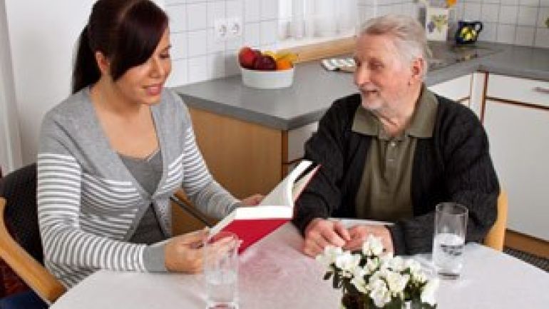 copyright: BilderBox.com Eine jüngere Frau liest einem älteren Mann etwas aus einem Buch vor.