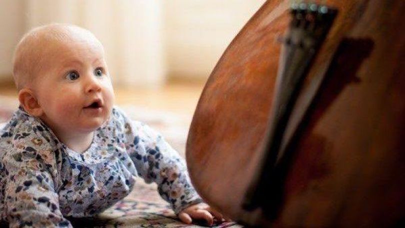 copyright: Julia Wesely Ein Baby krabbelt auf einem Teppich und blickt fasziniert auf ein Cello, das gerade gespielt wird