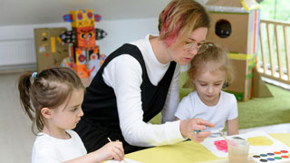 Eine Kindergrtnerin zeigt zwei Mdchen das Malen mit Wasserfarbe