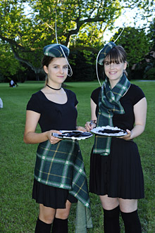 Zwei junge Frauen mit schwarzen Kleidern und karierten Mtzen und Schal beziehungsweise Umhang