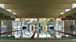 Schwimmbecken mit abgetrennten Bahnen, am gegenberliegenden Beckenrand stehen blaue und gelbe Liegen