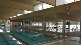 Schwimmbecken mit Beckenlift, im Hintergrund ein kleineres Becken mit gelben und blauen Liegen am Beckenrand