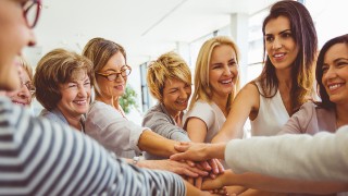 Mehrere Frauen stehen lachend im Kreis und legen ihre Hnde bereinander