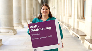 Frau hlt ein Plakat in die Hhe mit der Aufschrift: "Weltmdchentag - 11. Oktober - Mdchen gehrt die Welt!"