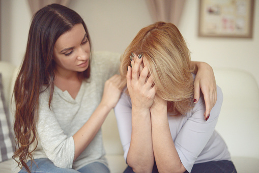 Eine Frau tröstet eine andere Frau, die die Hände vors Gesicht geschlagen hat.