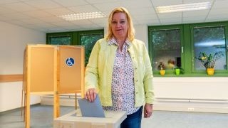 Frau steck blaues Kuvert in eine Wahlurne