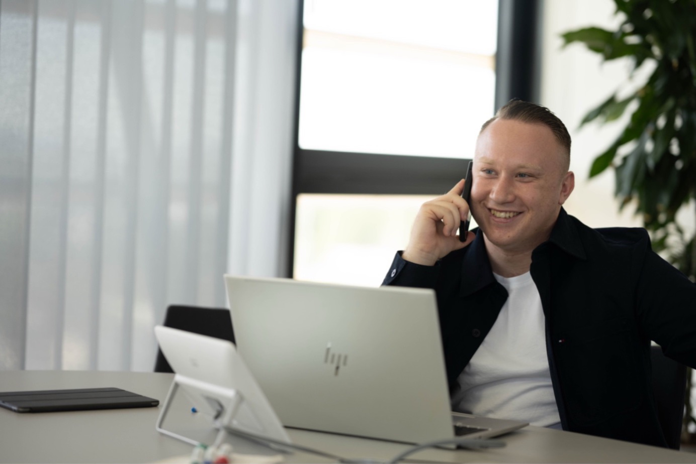 Mann am Schreibtisch telefoniert, vor ihm sein Laptop