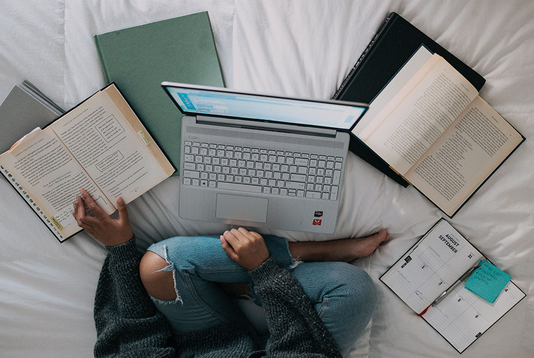 Mädchen lernt gerade und ist von einem Laptop und Büchern umgeben.