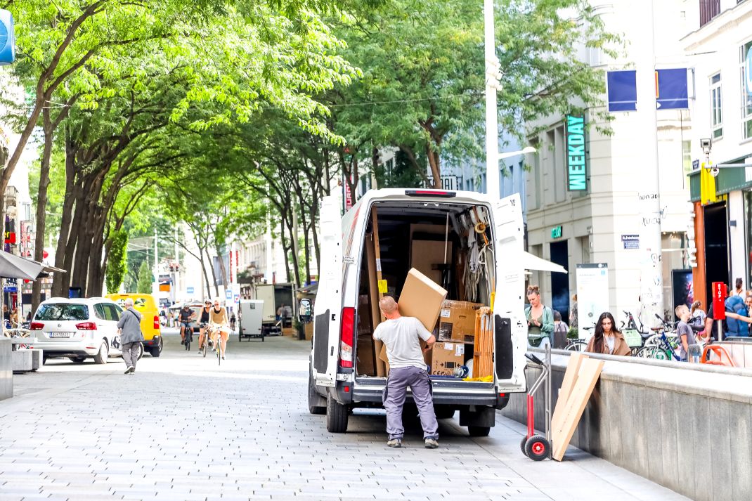 Eine Person belädt einen Transporter auf einer begrünten Straße.