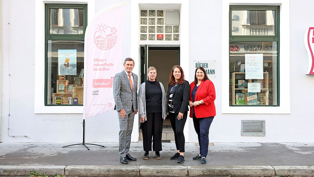 Four people in front of a shop marked ‘Bookshop’, with two display windows and a door in the centre. Three women and one man.