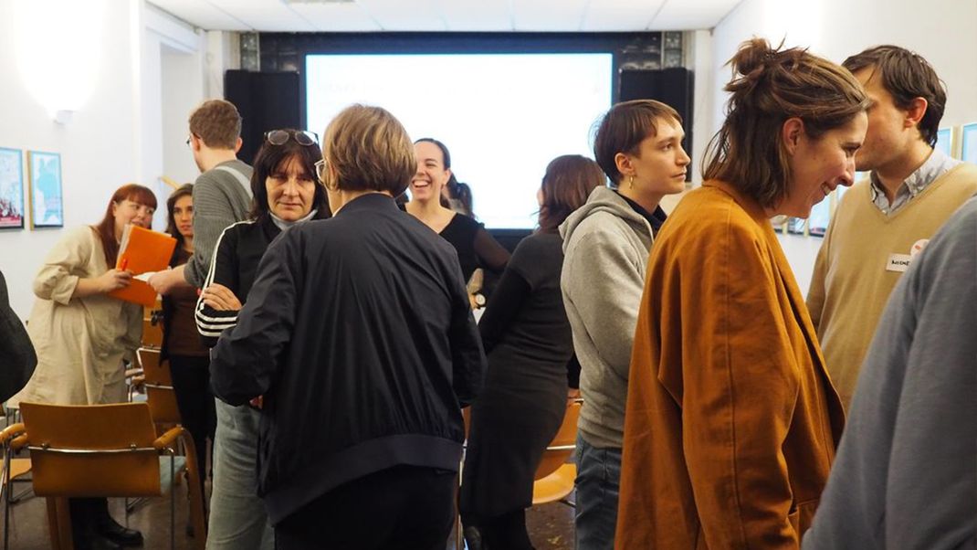 Photo of a workshop with younger prople standing and chatting with each other.