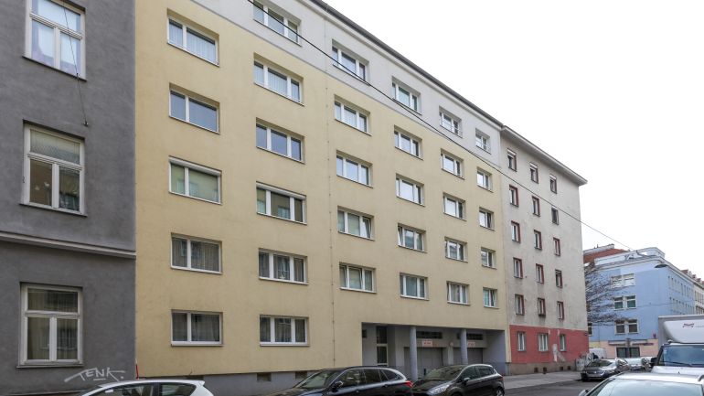 Exterior view of the house on Miesbachgasse. A five-storey building dating from the 1960s, with a beige façade and elongated windows.