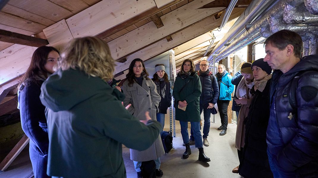 A photo of a group of visitors standing under a sloping roof, listening to a person in the foreground.