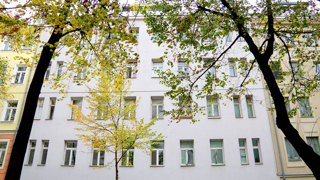 Exterior view of the Gründerzeit-style house at Ybbsstraße 6. Four storeys, a white façade and tall windows. In front of it are three trees with green foliage.