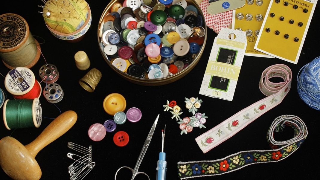A selection of colourful buttons and sewing kit laid out against a black background.