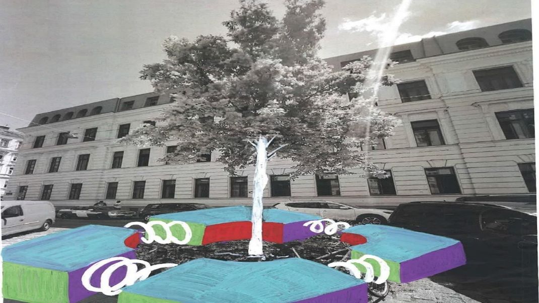 In the background is a long, two-storey Gründerzeit-style building in grey and white; in front of it stands a tree, also in grey and white, with a slender trunk painted white. Around this trunk are colourful seats, painted with light blue seat surfaces.