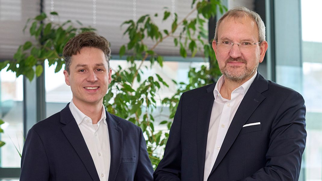 Gemeinsames Porträtfoto von Stephan Hartmann (links) und Otto Eckl (rechts in dunklen Sakkos und weißen Hemden in die Kamera lächelnd.