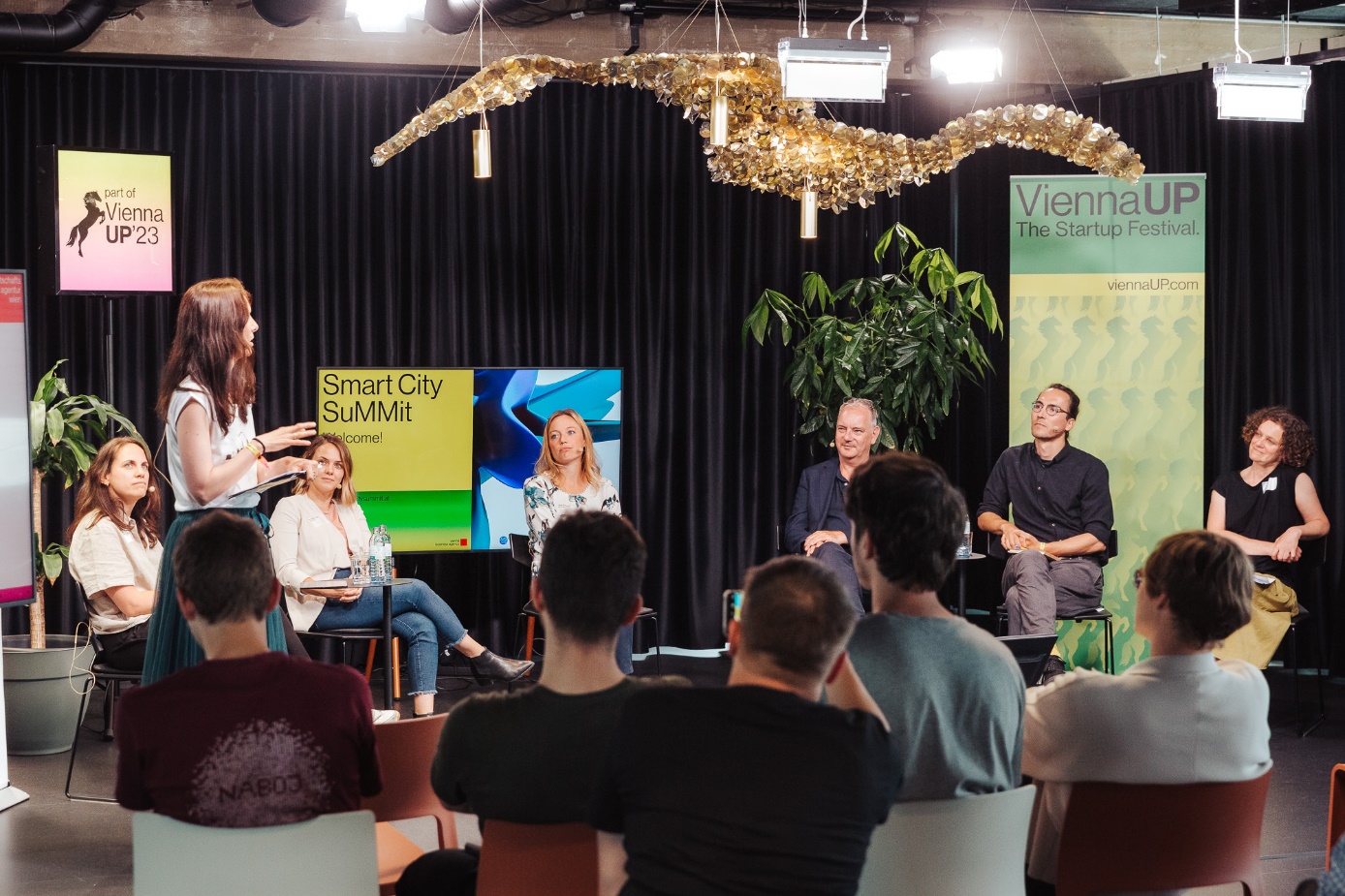 Smart City SuMMit 2023, Climate Lab

Six panelists are shown at the centre of the photo, with the moderator to the left and spectators seen from behind. Roll-up posters saying "ViennaUP" and "Smart City SuMMit" are shown against a black background.