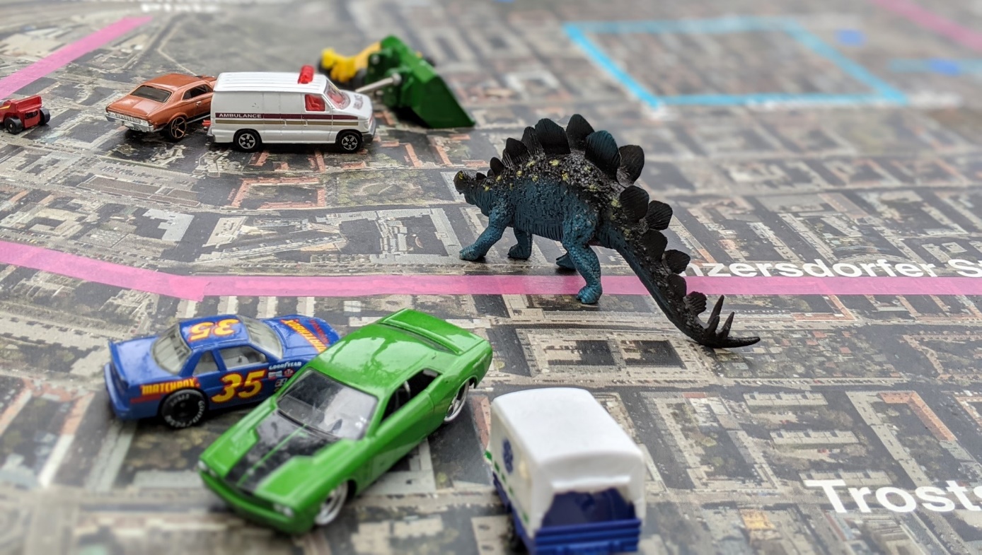 "Wohnstrassenleben" event

Matchbox toy cars creating a traffic jam on a city map, with same-size dinosaur toy figures 