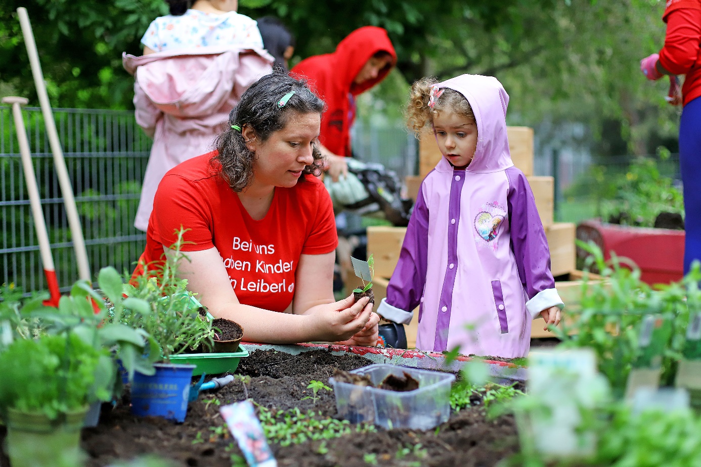 Healthy snacking in the park

A mother wearing a red T-shirt and a young girl wearing a lilac raincoat are gardening together on a raised bed.   