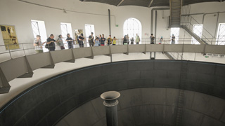 Eine Gruppe von Menschen steht vor einem Gelnder im Inneren des Wasserturms, im Vordergrund ist ein vertikales Rohr in der Mitte des Turms zu sehen